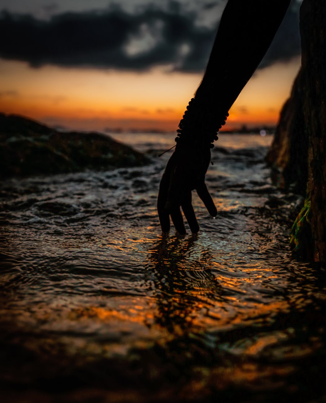 silhouette of person s hand touching water during sunset